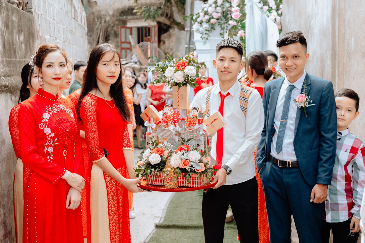 Group wearing traditional ao dai at a wedding procession, holding gifts.